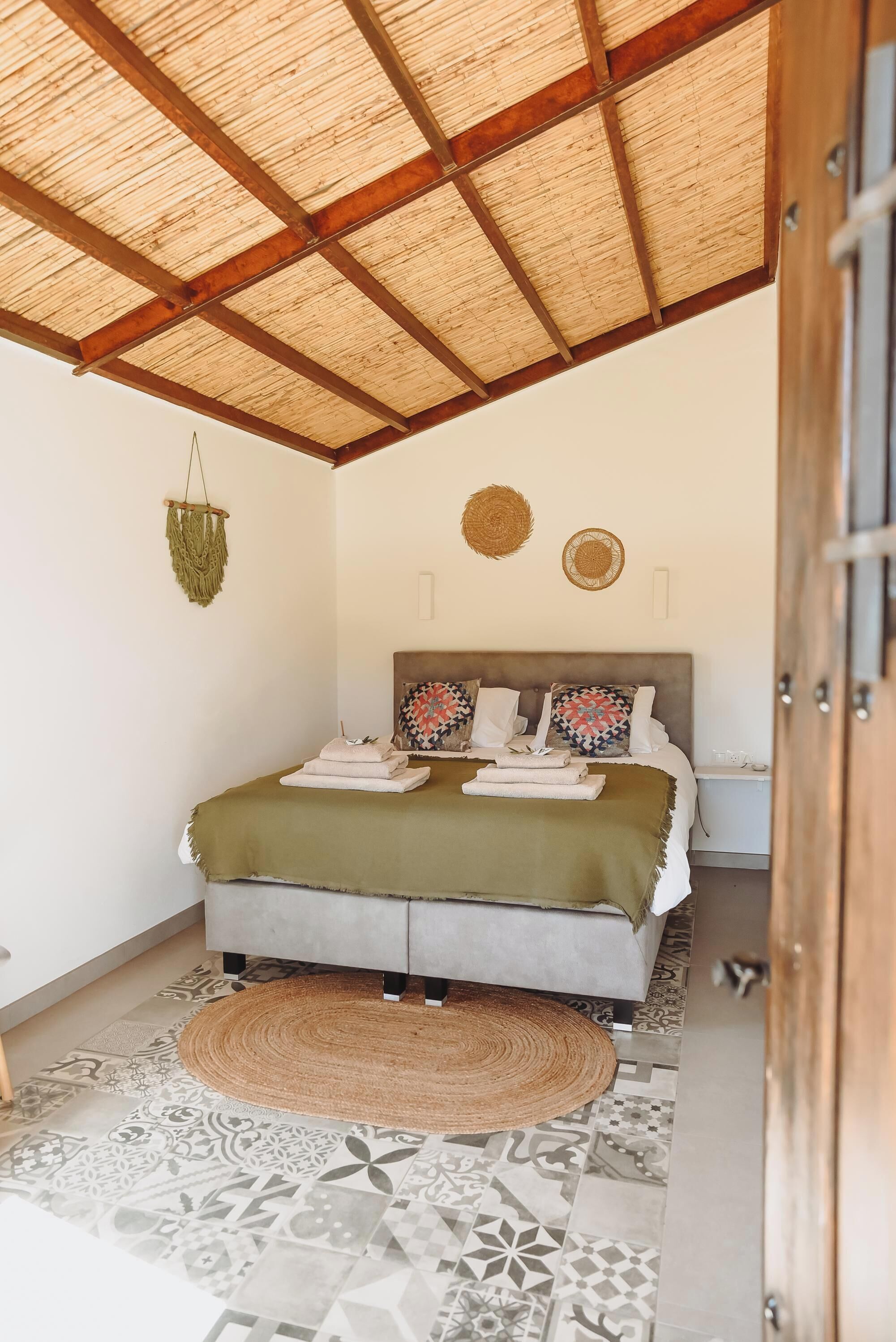 A bedroom with a bed, a woven ceiling, a patterned floor, and a small bedside table.