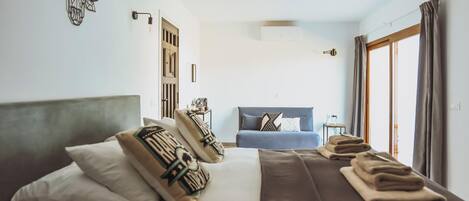 Ein Hotelzimmer mit einem großen Bett, einer Schlafcouch, einer Wandklimaanlage und einem Fenster mit Vorhängen.