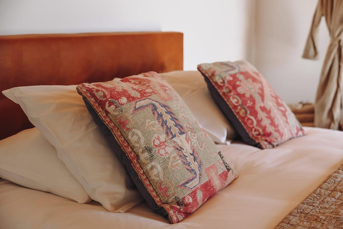 A bed with a wooden headboard, two patterned pillows, and a woven blanket.