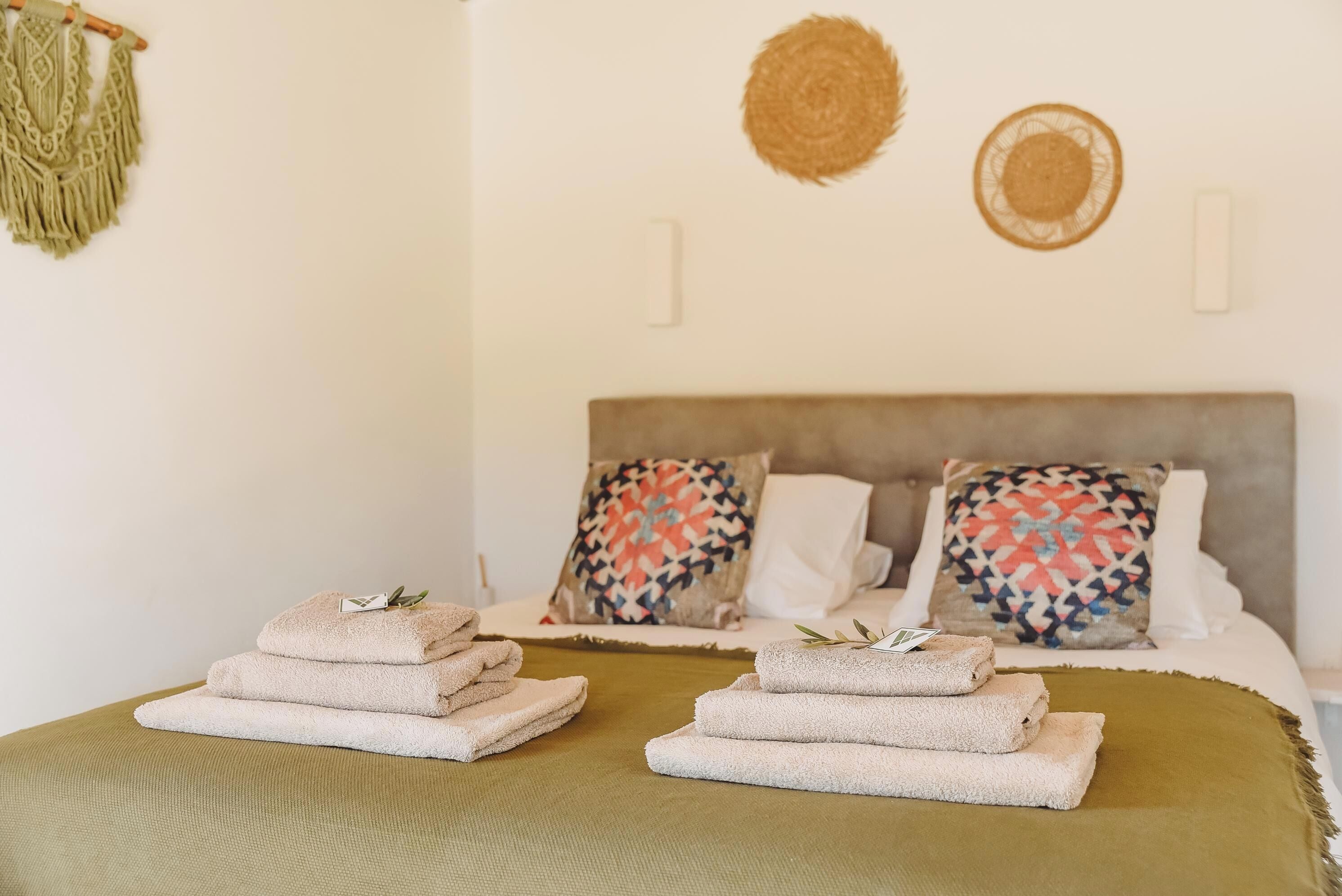 A neatly made bed with two pillows, a green throw blanket, and a stack of folded towels on the side.