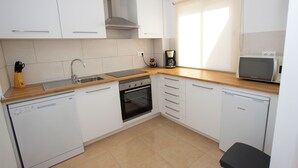 A compact kitchen with white cabinets, a dishwasher, an oven, a microwave, and a sink. - Ferienwohnung mit Pool und Herrlihem Garten (Mutxamel)