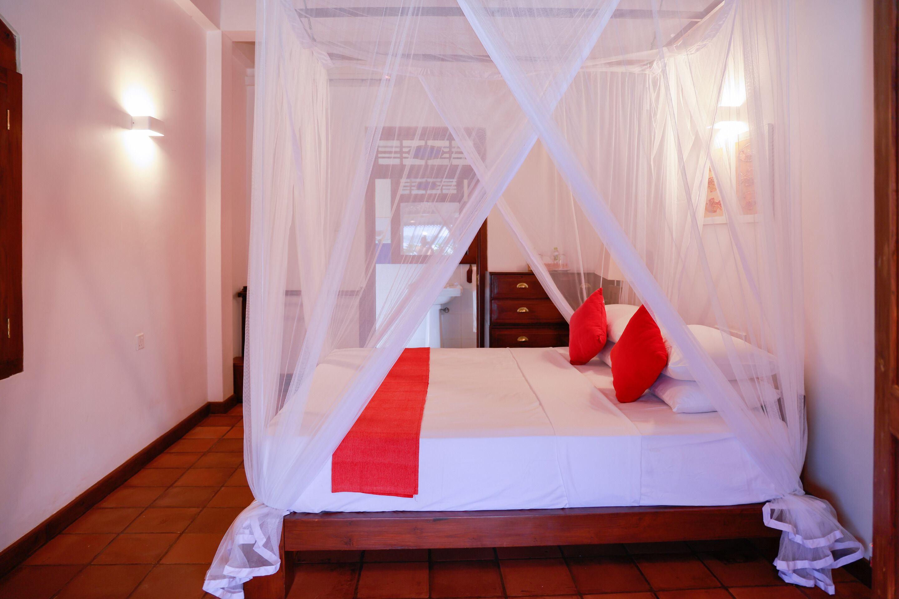 A bed with a white canopy and red pillows, a red runner, and a wooden headboard.