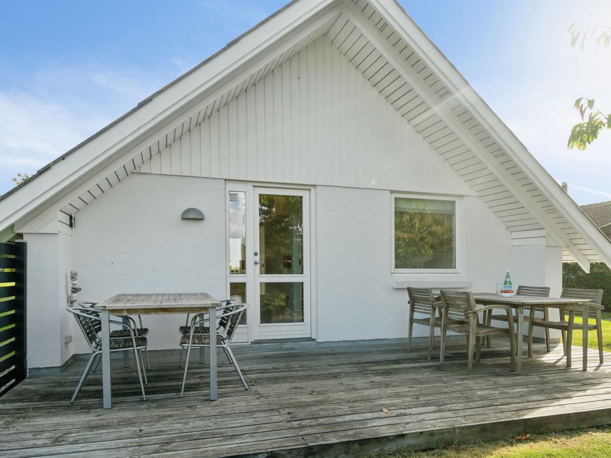 A white building with a sloped roof, a covered patio with a table and chairs, and a large window.