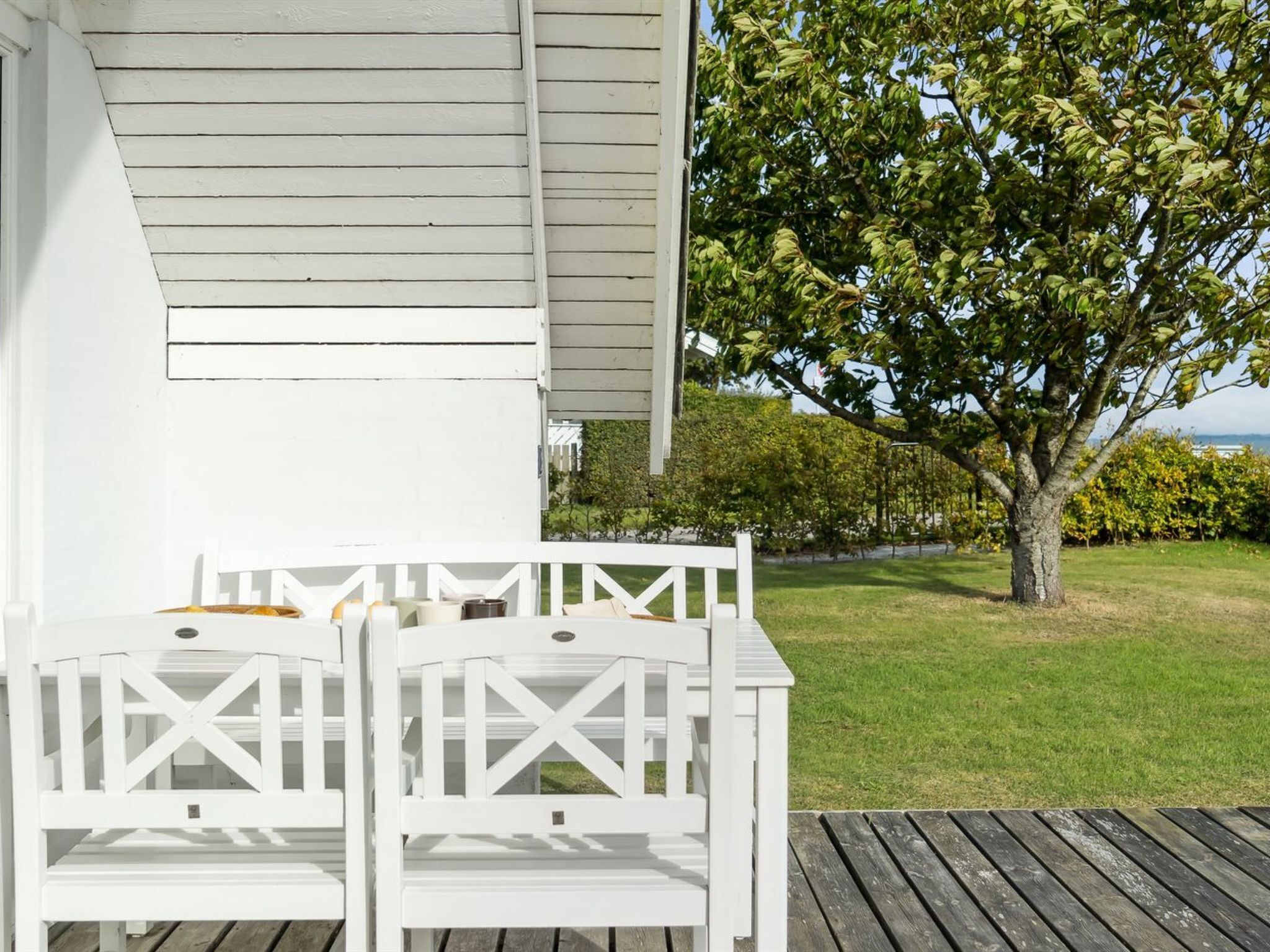 Une terrasse en bois peinte en blanc, avec deux chaises Adirondack blanches et une petite table.