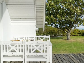 Um deck de madeira branca com duas cadeiras Adirondack brancas e uma pequena mesa.