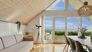 A modern room with a wooden ceiling, a sofa, a dining table with chairs, a telescope, and a view of the ocean. - "Jolanta" - 20m from the sea by Interhome (Malling)
