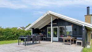 Una casa moderna con terraza de madera, mobiliario exterior y un ventanal grande.