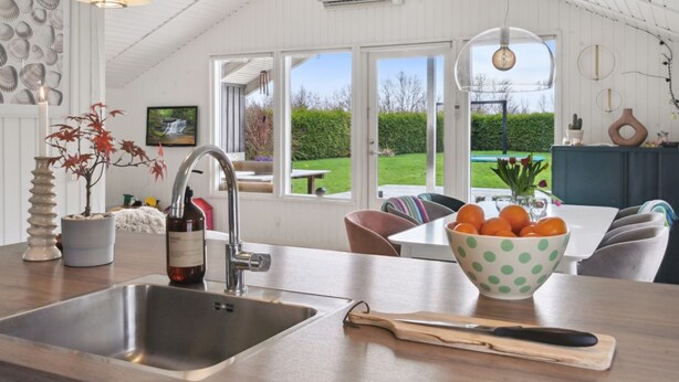 Una cocina moderna con un lavamanos grande, un comedor con vistas al jardín y un techo con vigas a la vista.