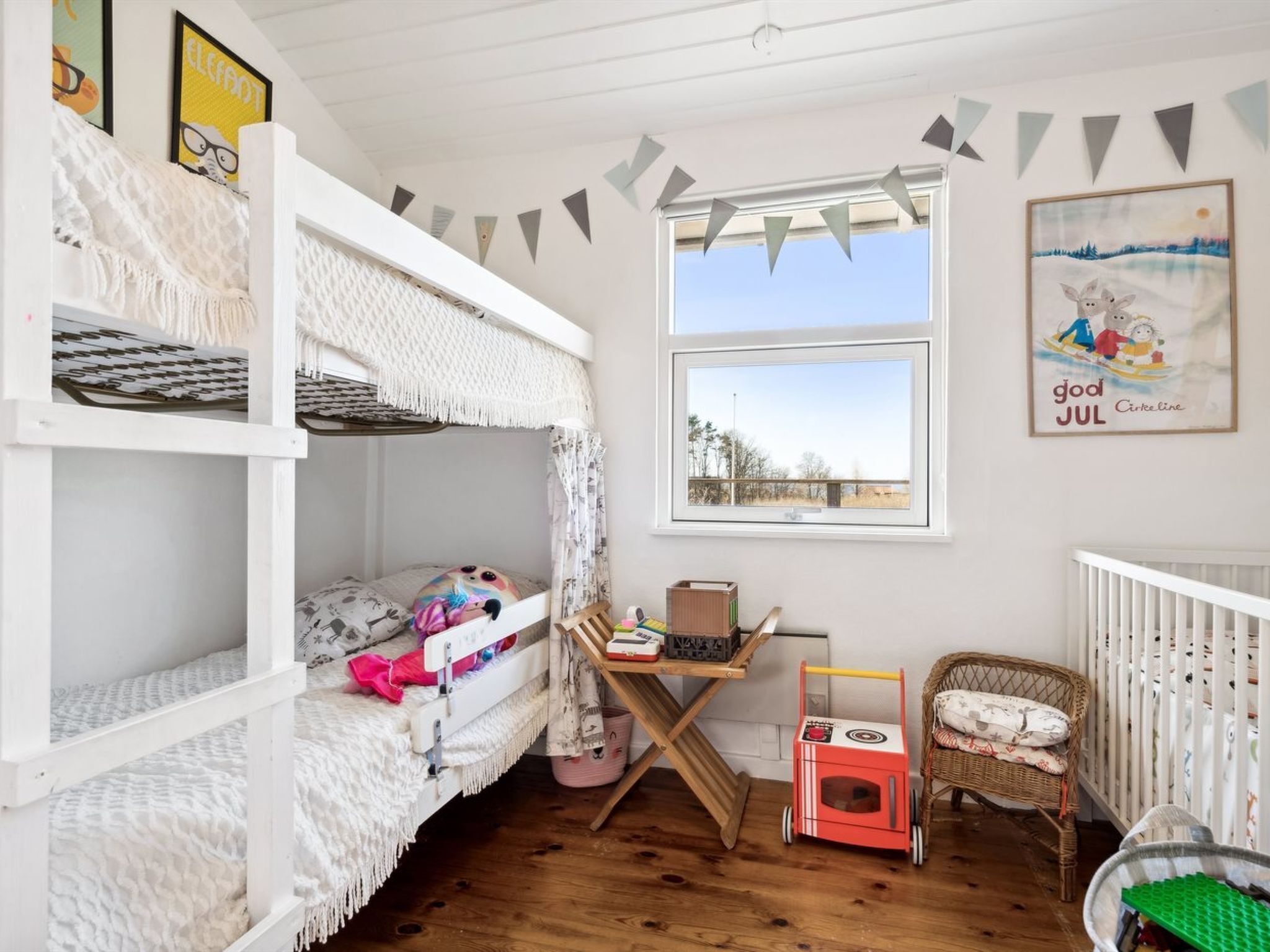 Een kinderkamer met stapelbedden, een bureau, een klein tafeltje, een ledikant en een raam met uitzicht.
