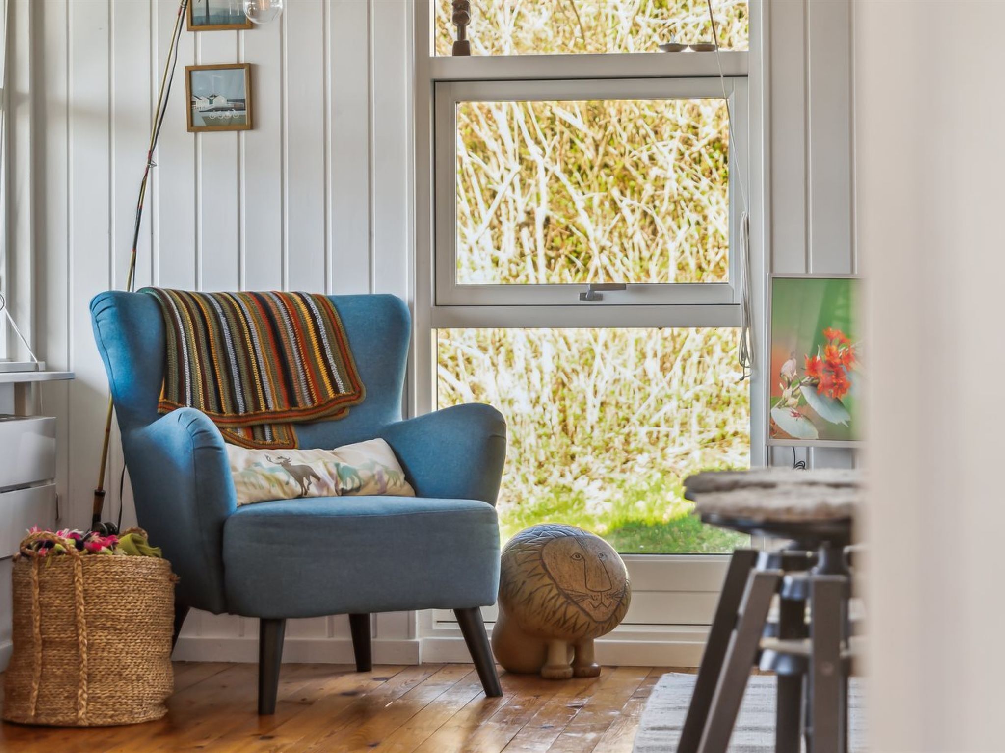 Ein Zimmer mit blauem Sessel, einem gewebten Korb, einer dekorativen Löwenskulptur und einem Fenster mit Blick auf Bäume.
