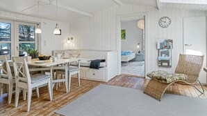 Une chambre moderne aux tons clairs, avec un espace repas, un lit et un fauteuil en osier.