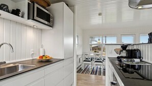 Una cocina moderna con armarios blancos, un lavamanos de acero inoxidable, un microondas y una cafetera.
