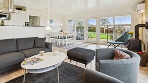 Una sala de estar moderna con un sofá gris, una mesa de centro blanca y un comedor con sillas y una mesa blancos.