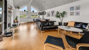 Un vaste espace de vie doté d’un haut plafond, comprenant un coin repas et un coin salon avec un canapé et des fauteuils.
