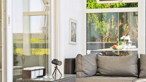 Un espace extérieur accueillant avec un canapé en osier et une table à plateau de verre, un télescope et une vue sur la verdure grâce à de grandes fenêtres.