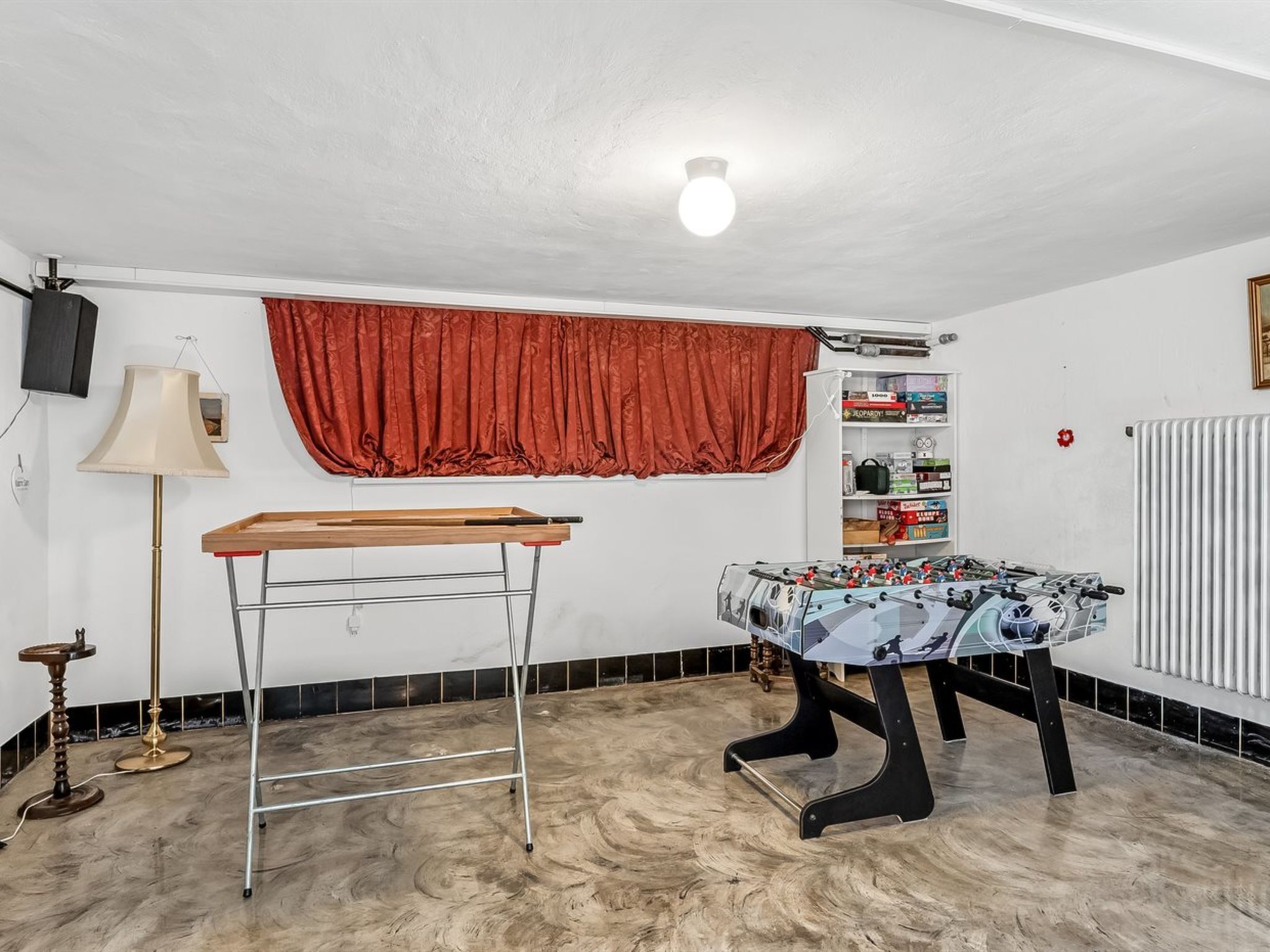 Une pièce équipée d’un baby-foot, d’un bureau réglable en hauteur, d’une lampe et d’une étagère remplie de jeux de société.