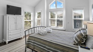 Un dormitorio con una cama, un televisor sobre un mueble y ventanas amplias.