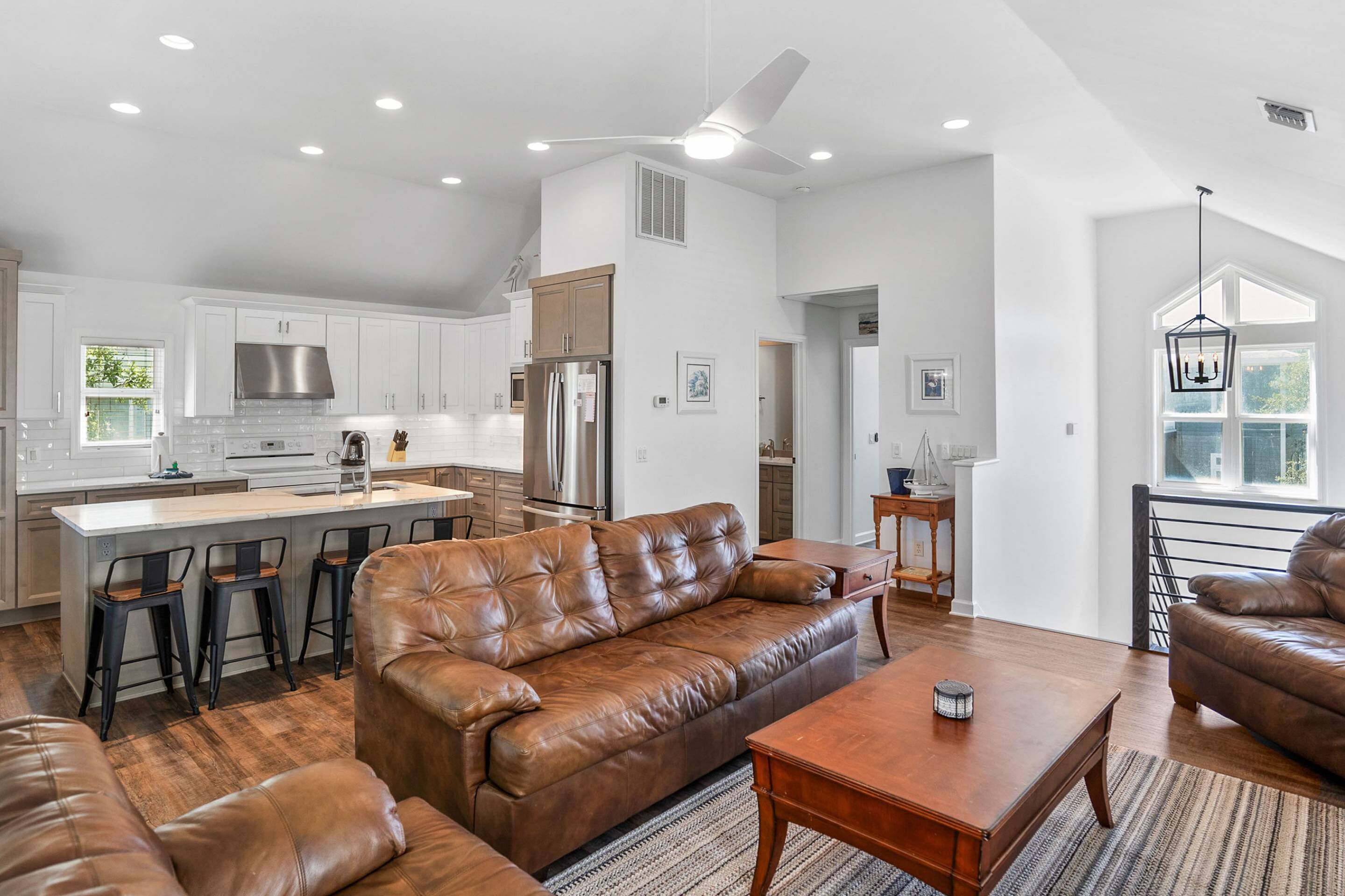 A spacious living area with a brown leather sofa, wooden coffee table, and a kitchen with white cabinets and a central island.