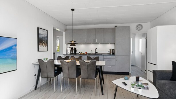 A modern kitchen with grey cabinets, a dining area with a round table and chairs, and a living area with a sofa and a coffee table.