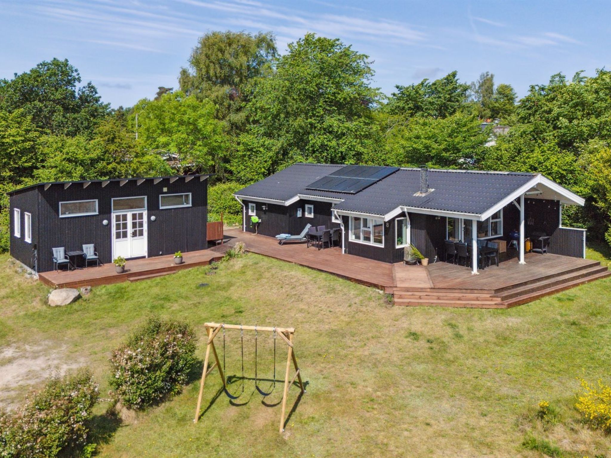 A two-story house with a deck and a swing set in the yard.