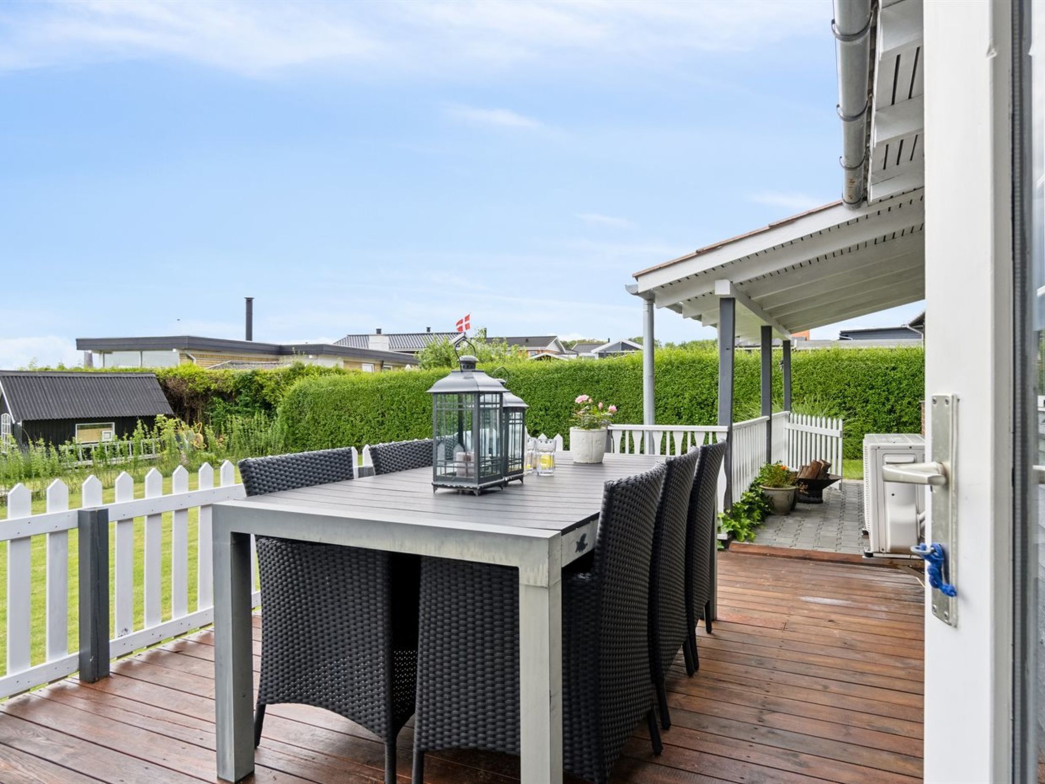 An outdoor deck with a table and chairs, a lantern, and a white picket fence.