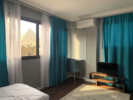 Habitación de hotel con cama, escritorio, televisor y vista a una pirámide desde la ventana.