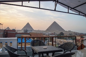 A balcony with a view of two pyramids, a table, and chairs.