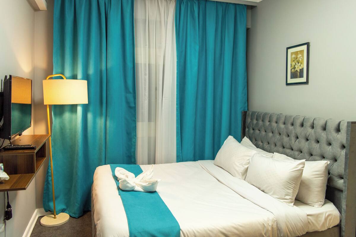 A hotel room with a bed, a bedside table with a lamp, a mirror, and a picture on the wall.