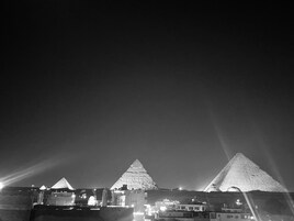 A nighttime view of the pyramids with surrounding buildings and a clear sky.