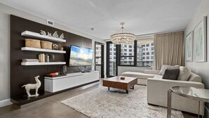 A modern living room with a large flat-screen TV, a chandelier, a sofa, a coffee table, and a fireplace. - Luxury Beachfront Condo / Resort / 1415 (Miami Beach)