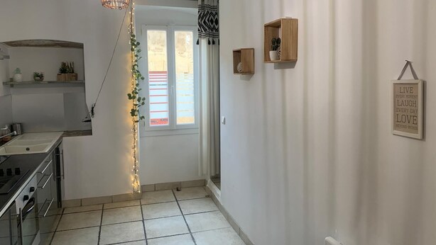 A kitchen with a modern stove, a hanging light fixture, and a window with striped blinds. - Charming house (Remoulins)