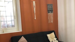 A room with a black sofa, a small white table with a potted plant, and two wall hangings. - Charming house (Remoulins)