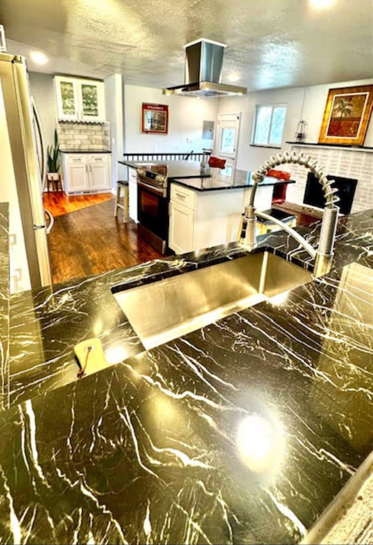 A kitchen with a black marble countertop, white cabinets, and a stainless steel range hood.