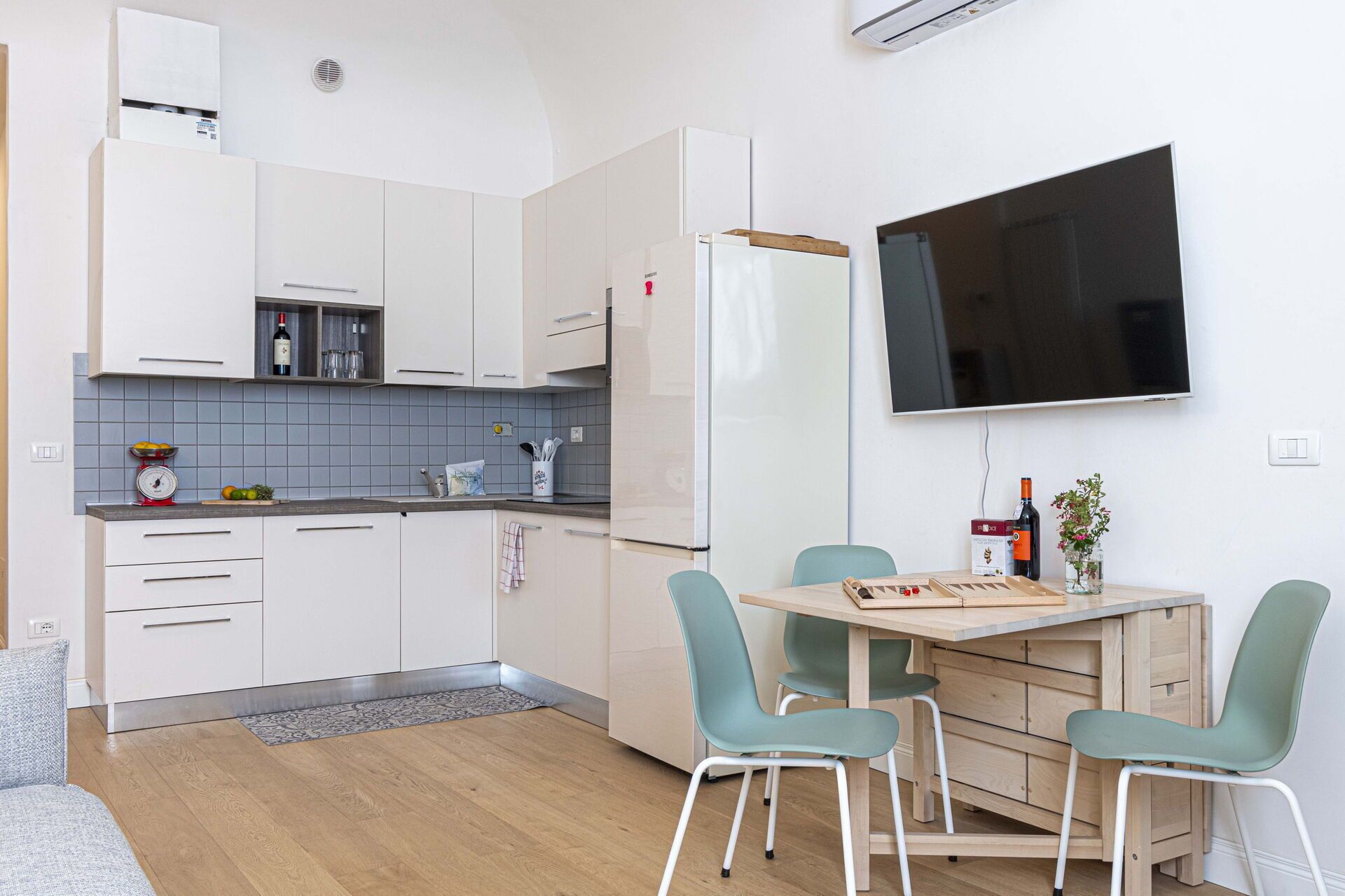 A modern kitchen with white cabinets, a built-in fridge, and a dining area with two chairs and a table.