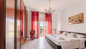 Une chambre à coucher avec un lit, une chaise, un tableau et une vue sur l’extérieur, visible à travers une porte.