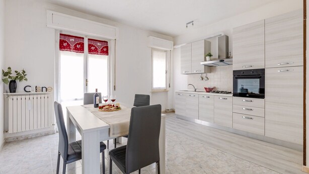 Une cuisine moderne avec des meubles blancs, un coin repas comprenant une table et des chaises, et un lambrequin décoratif rouge au-dessus des fenêtres.