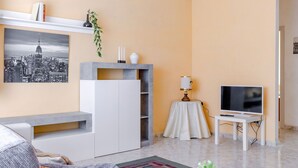 Un salon moderne avec un canapé, un téléviseur, une petite table avec une lampe et une bibliothèque.