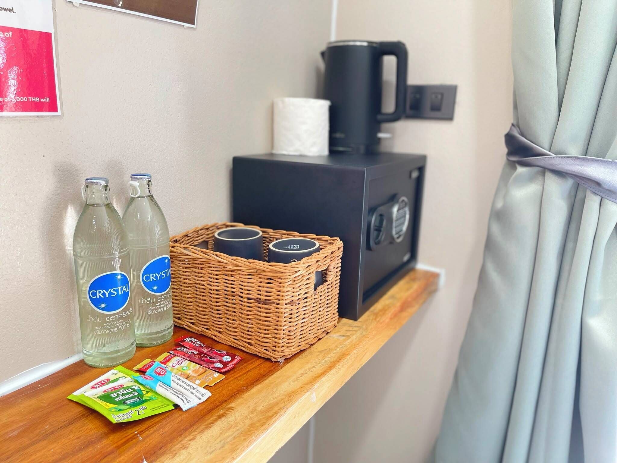 Une chambre d’hôtel avec une étagère en bois sur laquelle sont posées deux bouteilles d’eau, un panier contenant deux tasses, une machine à café et une boîte de mouchoirs.