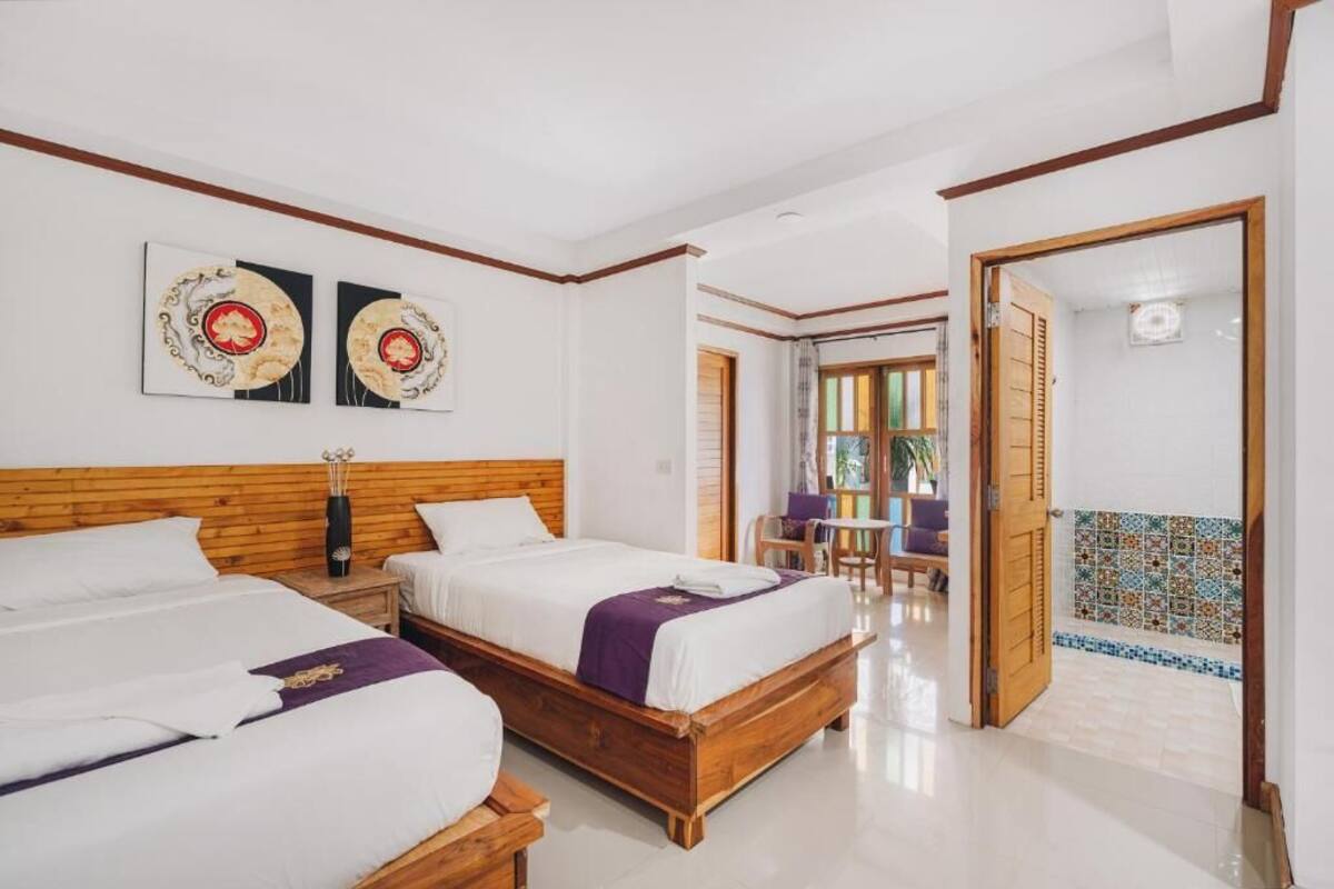A hotel room with two beds, a wooden headboard, and a hallway leading to a dining area.