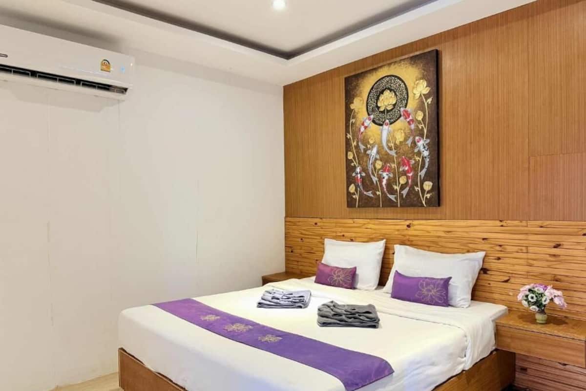 A neatly made bed with white and purple bedding, a wooden headboard, and a wall-mounted air conditioner.