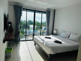 Habitación de hotel con cama, escritorio, silla, televisor y vistas al exterior.