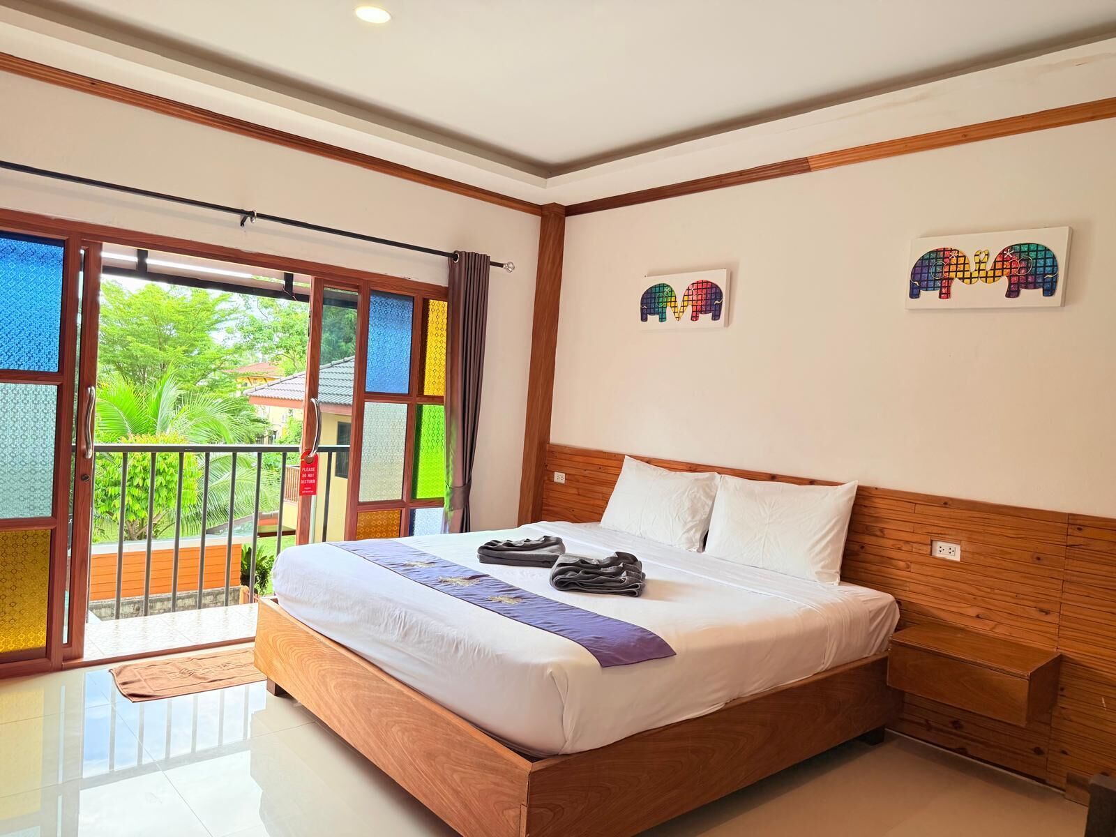 Une chambre d’hôtel avec un grand lit, une tête de lit en bois et un balcon offrant une vue sur la verdure.