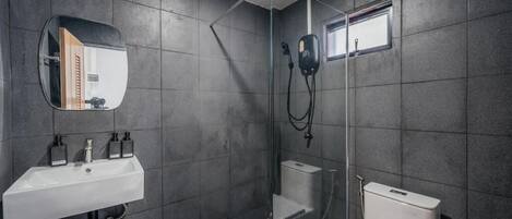 Un baño moderno con ducha de vidrio, un lavamanos blanco con dispensadores de jabón y un inodoro.