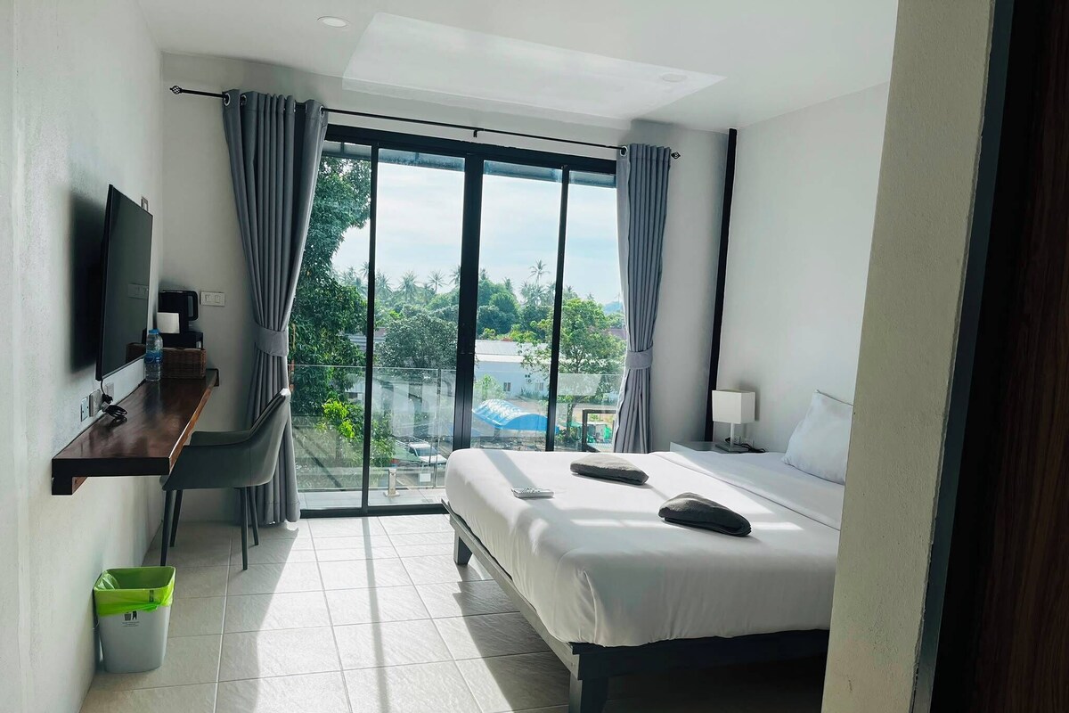A hotel room with a bed, a desk, a television, and a view of the outdoors.