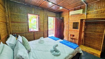 Une pièce comprenant un lit, deux fenêtres, une porte et un climatiseur fixé au mur.