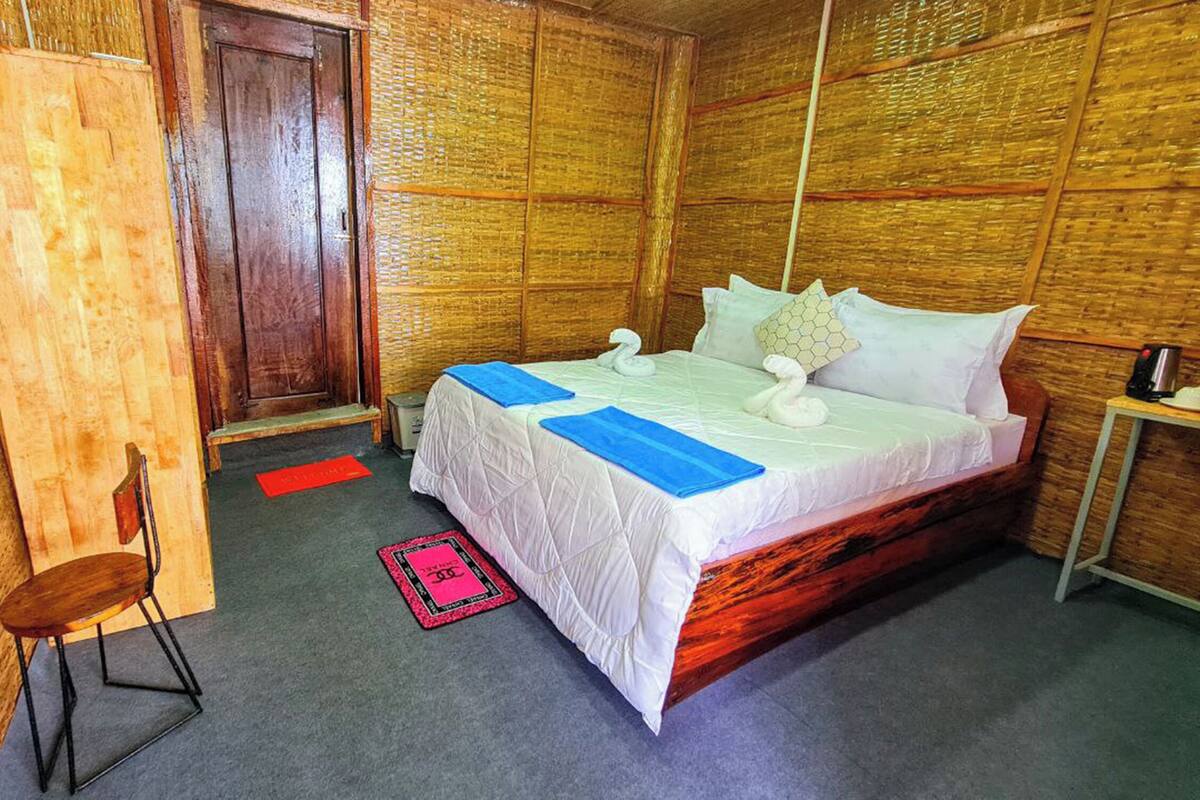 A room with a wooden bed, a chair, a small table, and a door.