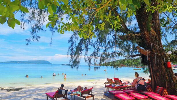 A beach with clear blue water, people swimming and sunbathing, and a large tree providing shade. - Europe Enchanted Bungalow Koh Rong (Koh Rong)