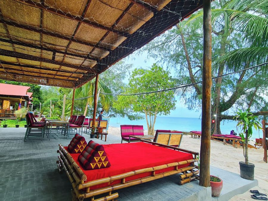 A beachside lounge with bamboo furniture, a red cushioned sofa, and a view of the sea.