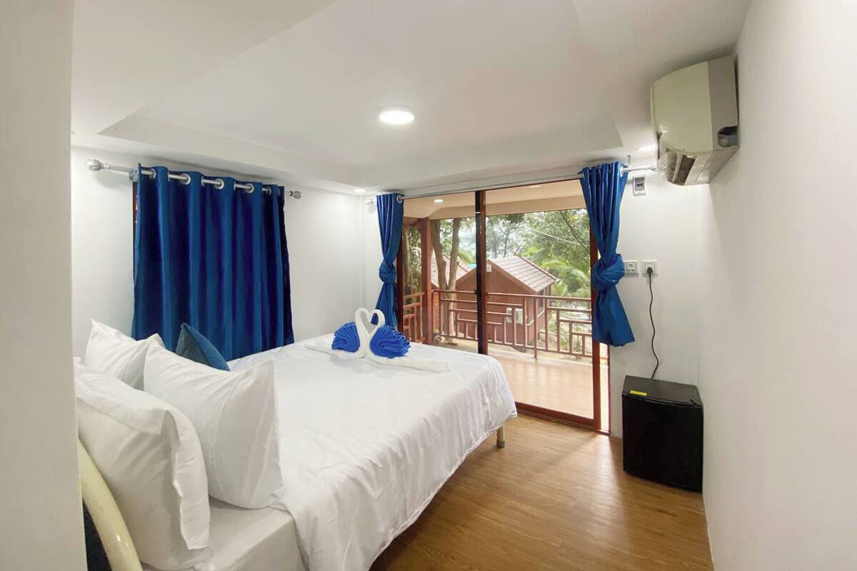 A hotel room with a bed, two blue curtains, a balcony with a view, and a black speaker.