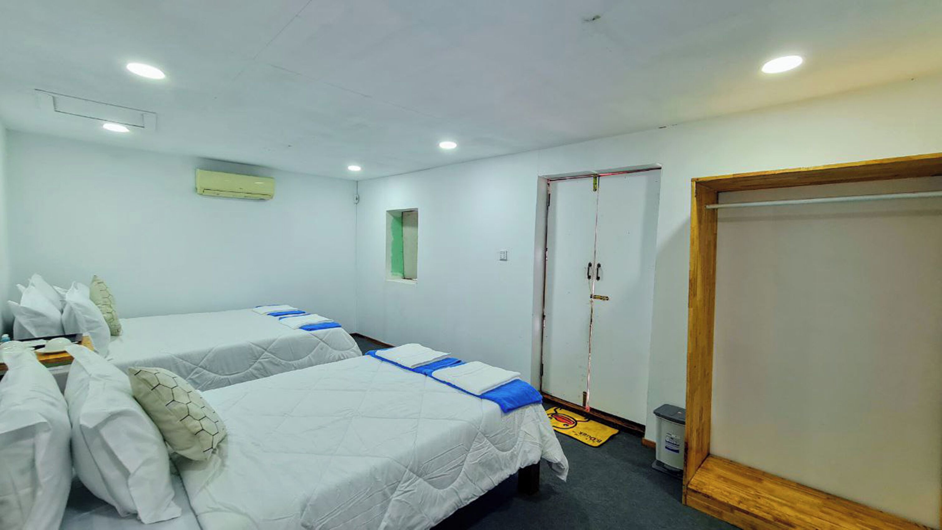 A hotel room with two beds, a wardrobe, and a small window.